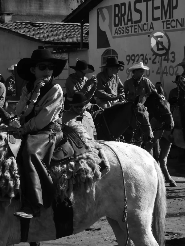 Fotografia em preto e branco, no formato vertical, mostrando um grupo de homens montados a cavalo em uma rua.
